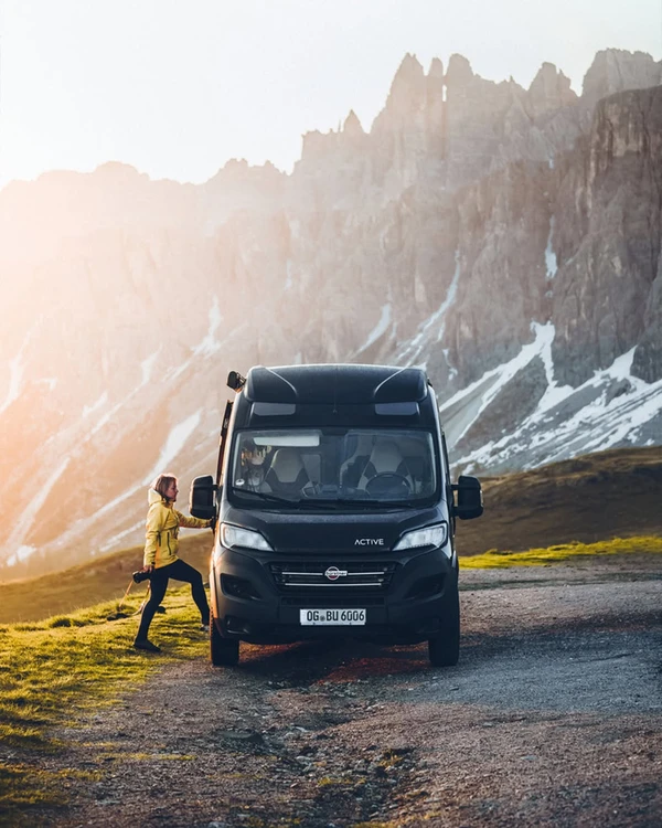 Camper negra en una carretera de montaña bajo picos rocosos escarpados.