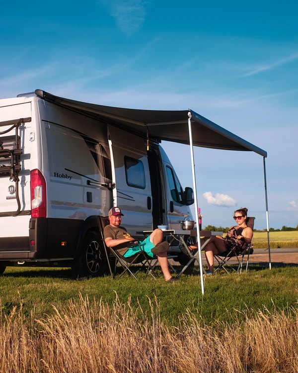 Pareja descansando en sillas de camping bajo el toldo de su autocaravana.