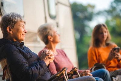 Tres mujeres descansando en sillas de camping delante de una autocaravana, con el sol de la tarde