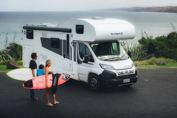 Dos surfistas con sus tablas junto a una autocaravana en la costa