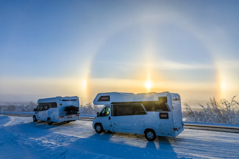 Dos autocaravanas en una carretera nevada, con un halo alrededor del sol de invierno