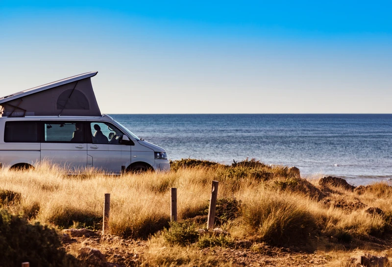 Camper con el techo elevable abierto, aparcada en las dunas junto al mar