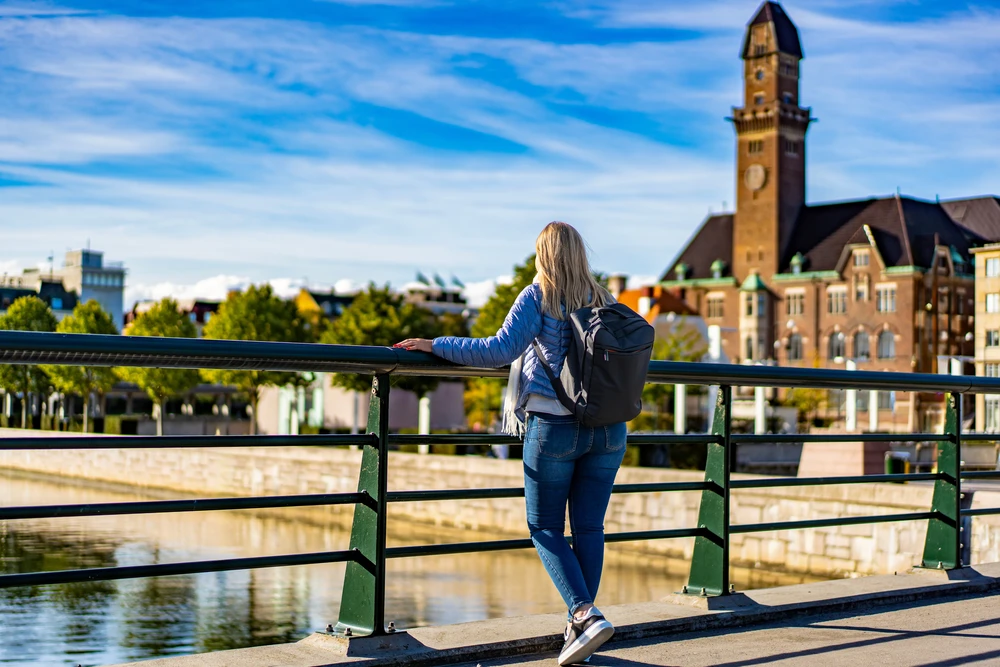 Viajera con mochila en un puente, mirando un edificio de ladrillo con torre de reloj