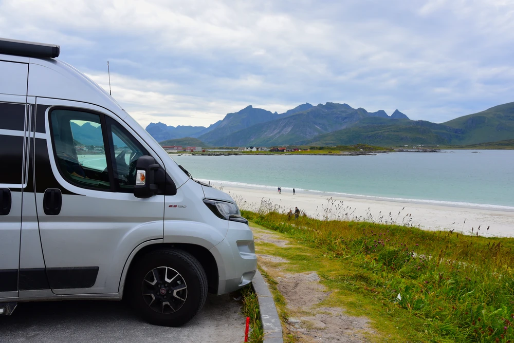 Camper aparcada junto a una playa de arena, con montañas al otro lado del agua