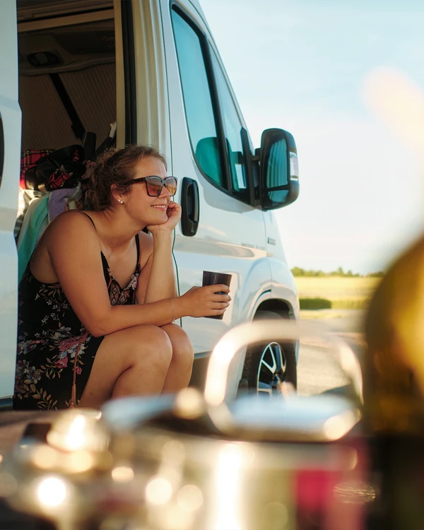 Mujer con una taza de café sentada en la puerta abierta de una camper