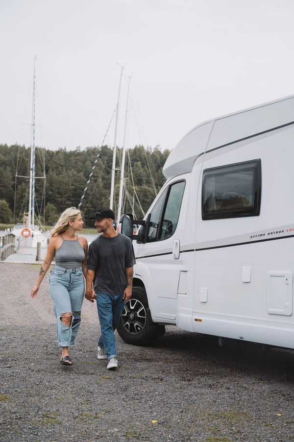 Pareja paseando de la mano junto a una autocaravana en un puerto