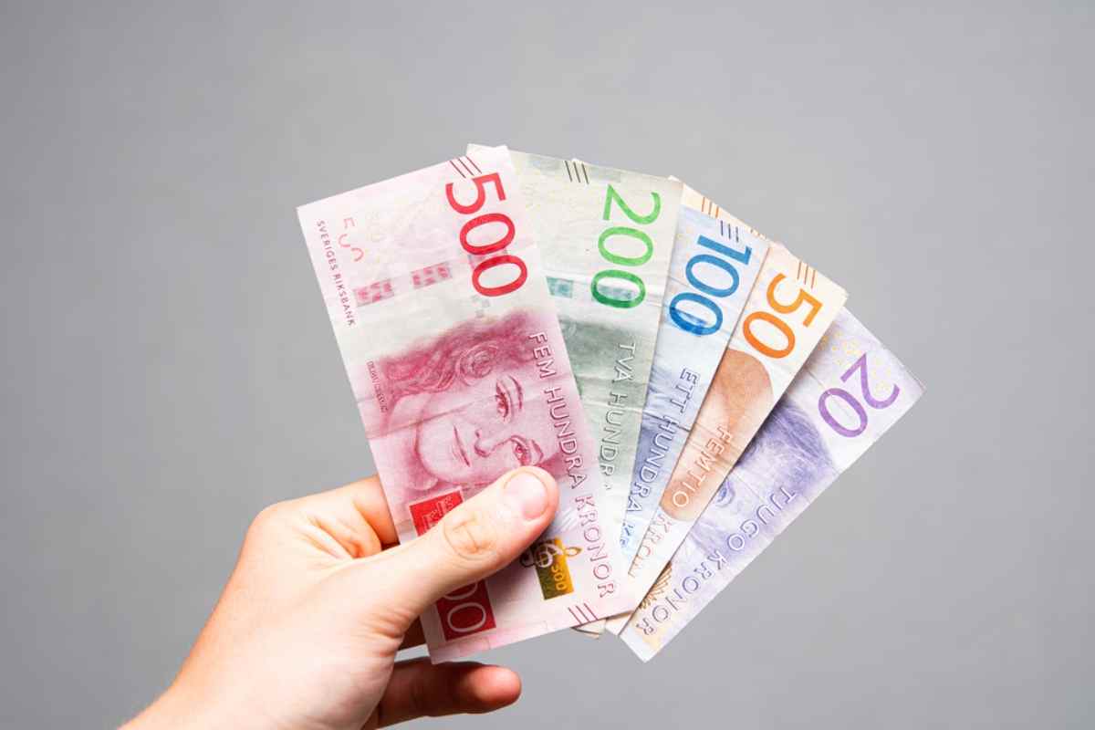 Hand som håller svenska sedlar (20–500 kronor) – budgettips för roadtrip i Sverige: räkna med bränsle, mat, camping och aktiviteter.