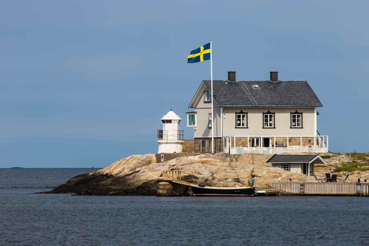 Fyr och kusthus med svensk flagga på klippa vid stilla hav – perfekt morgonstopp under roadtrip i Sverige för utsikt och foto.