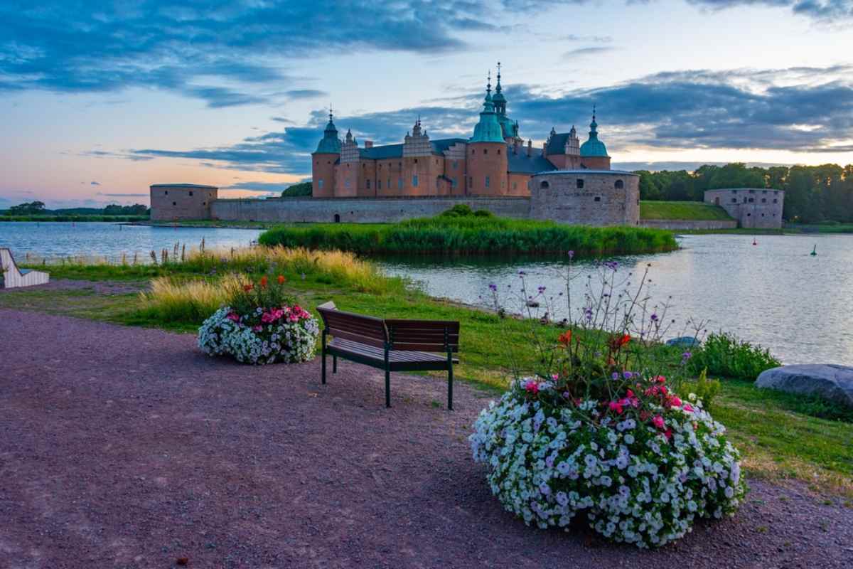Kalmar slott i kvällsljus vid vattnet, blomsterkrukor och bänk i förgrunden – kulturstopp på en roadtrip i Sverige.