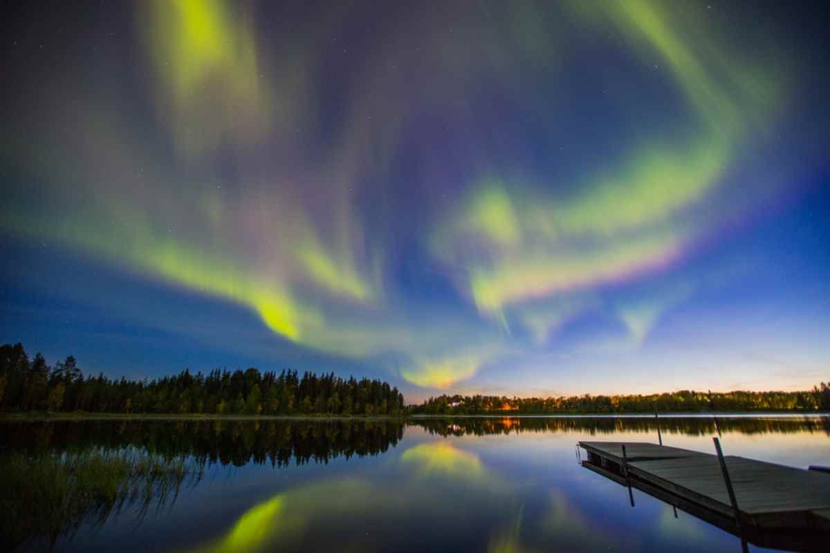 Norrsken som speglar sig i sjö med brygga och skog – magisk natt i Lappland under en vinter-roadtrip i Sverige.