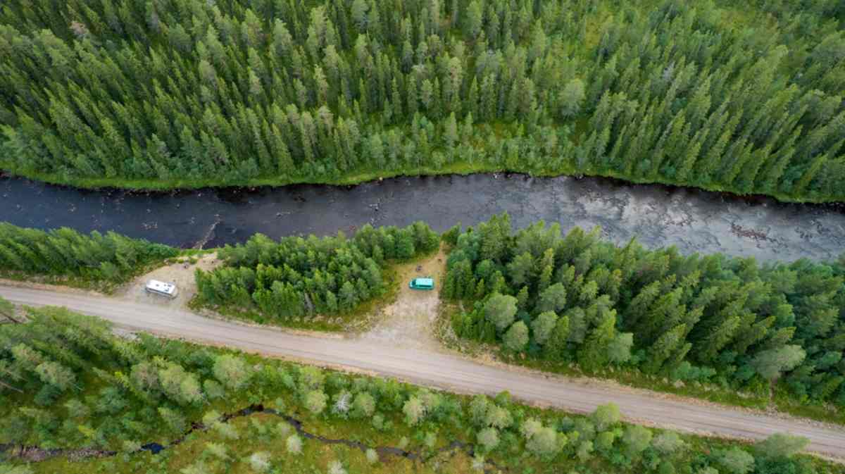 Drohnenaufnahme mehrerer Fahrzeuge, die in einem Wald nahe einem See parken.