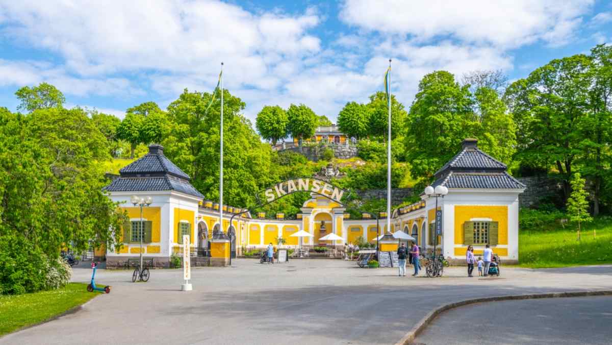 Allmän vy över huvudingången till Skansen i Stockholm, Sverige med en särskilt gul fasad och grön vegetation runtom.