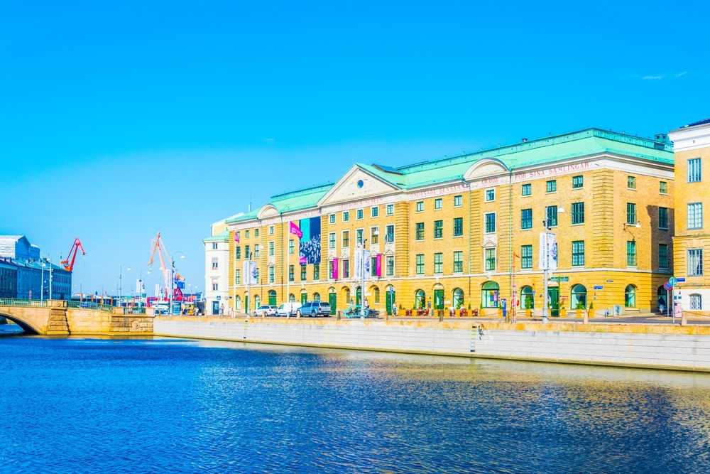 Overview of the yellowish façade of the City Museum of Gothenburg contrasting with the blue of the water in front of it and the sky.