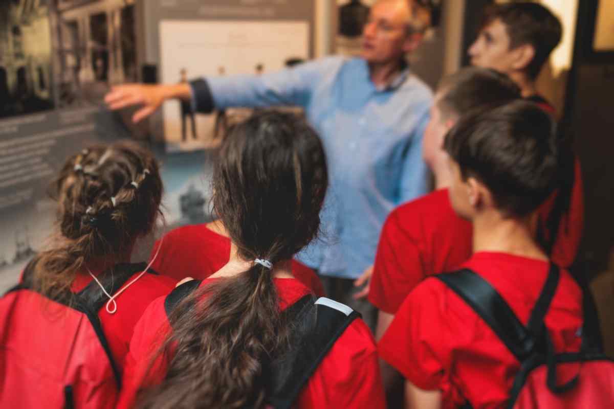 Close-up of a child wearing red clothing listening attentively to the instructions of an elderly man in what appears to be a museum.