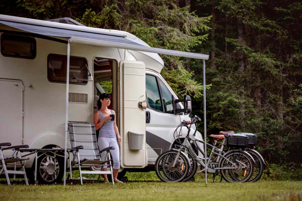 Cycling Infrastructure in Sweden A woman stands at the door of her white motorhome parked in a spot where chairs and bicycles are displayed outside.