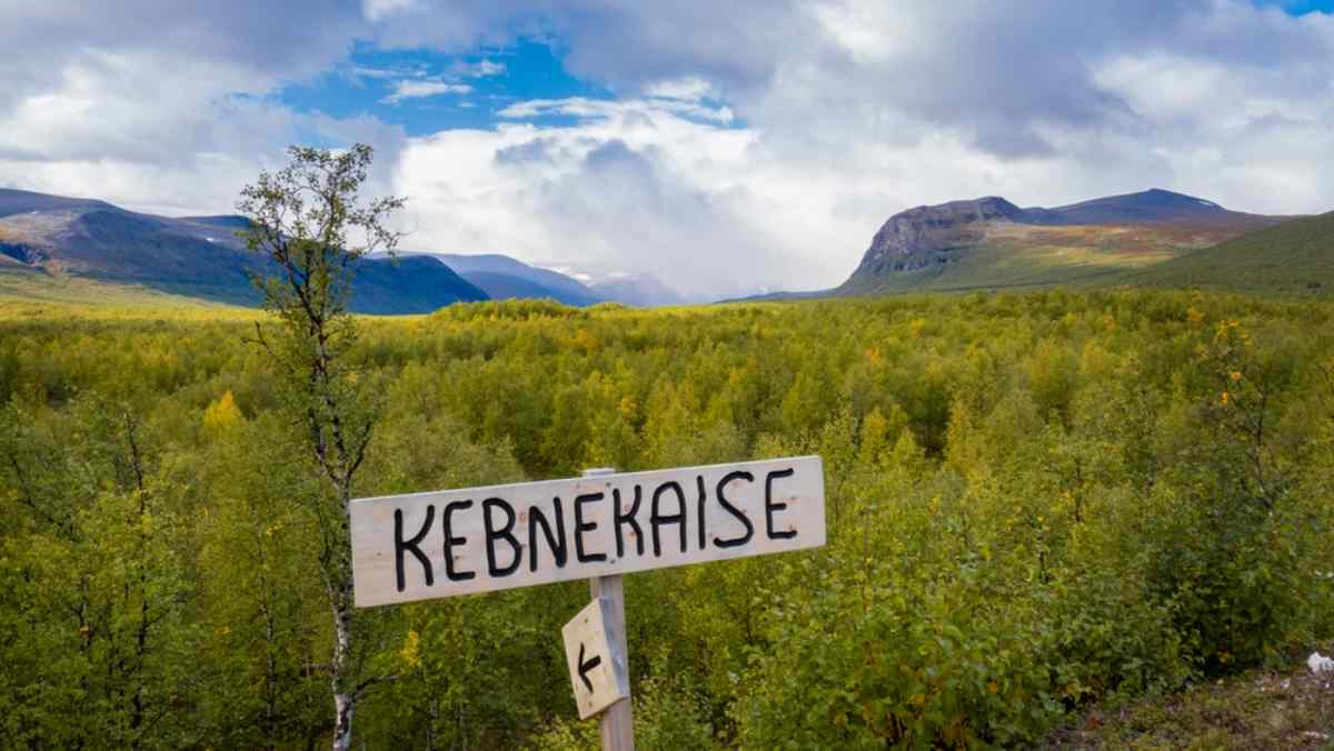 Detailansicht eines Holzschildes mit der Aufschrift “Kebnekaise” in einer schwedischen Naturlandschaft.