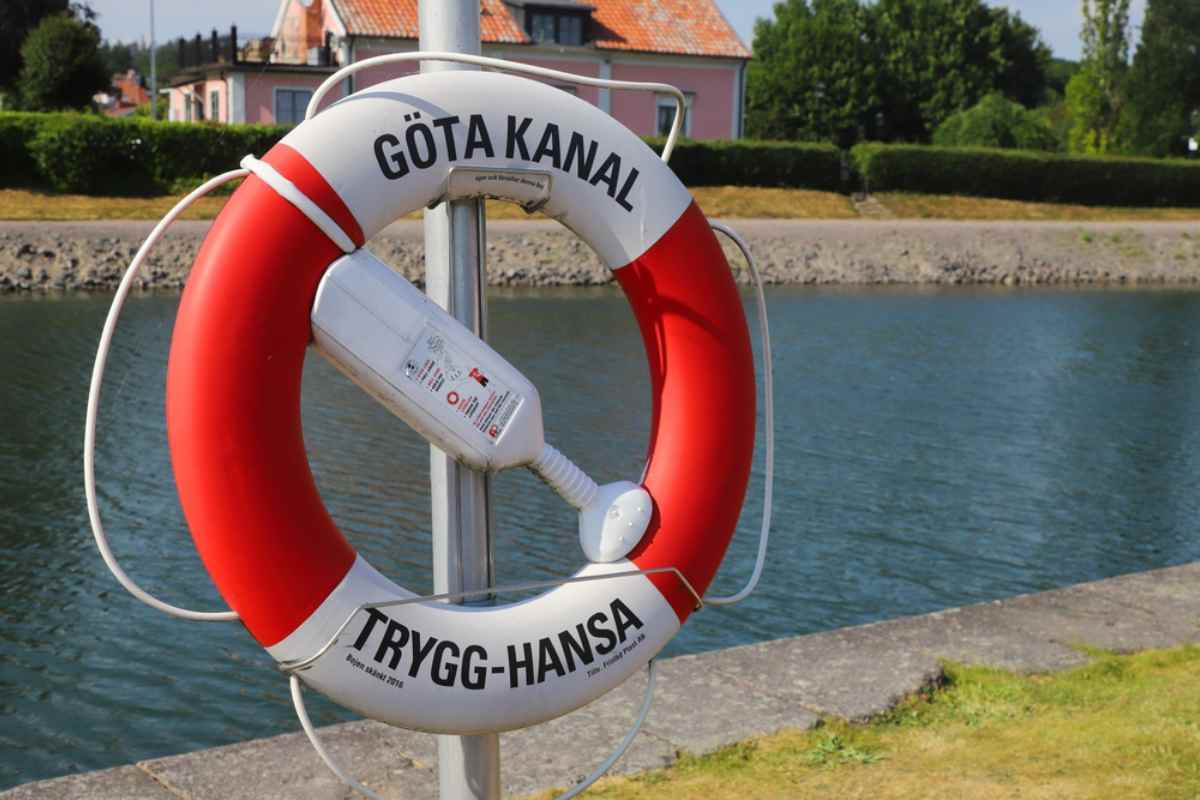 Närbild av en rödvit livboj märkt ”Göta kanal” och ”Trygg-Hansa” vid kanalen en solig sommardag.
