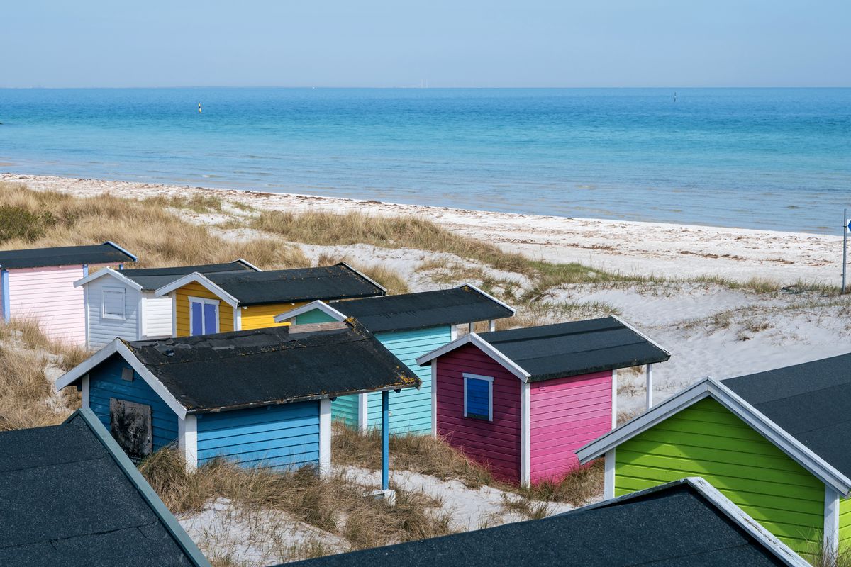 Drönarvy över färgglada hus mot den vita sanden på en strand i Skåne