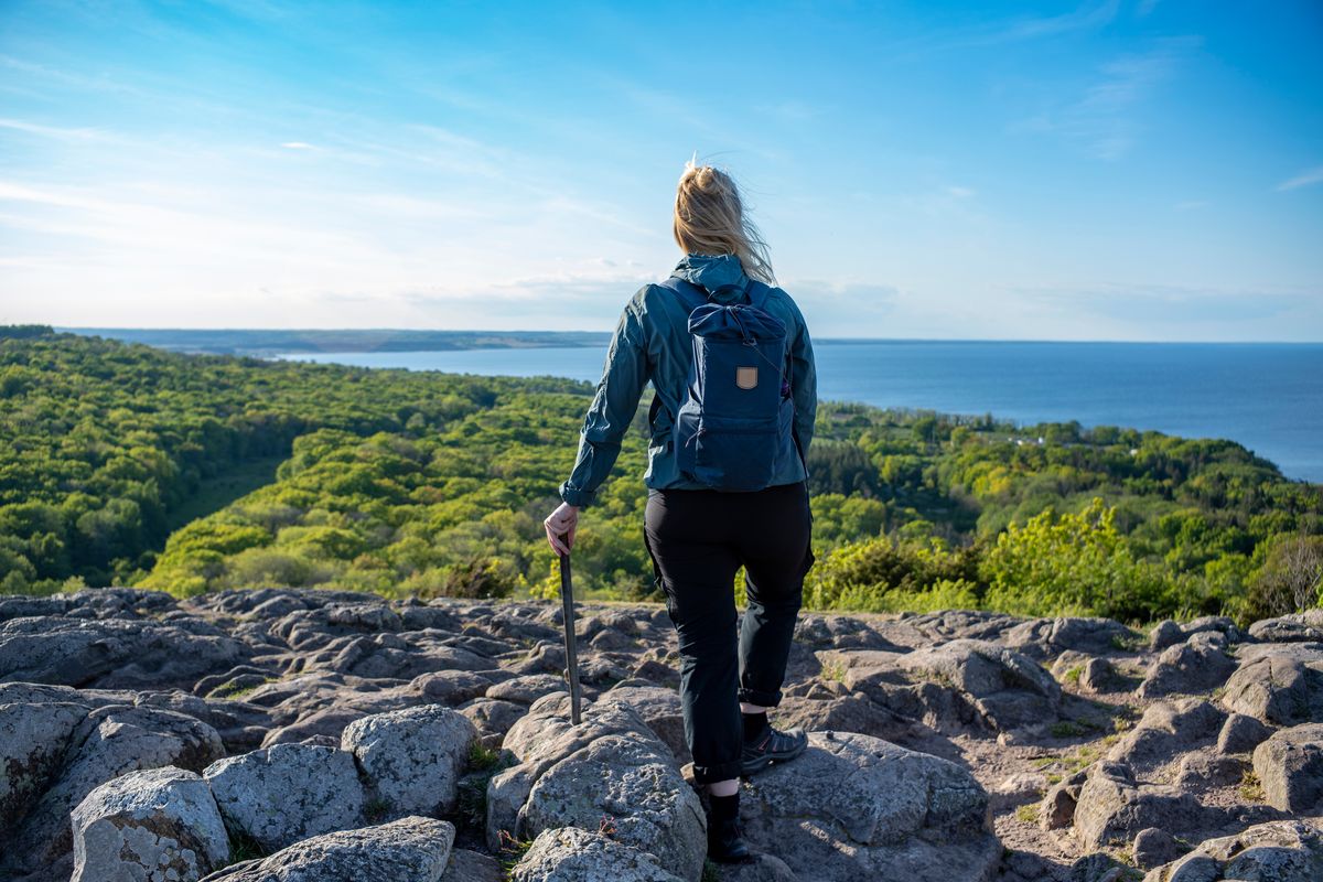 En kvinna i vandringsutrustning blickar ut över klippor i Skåne