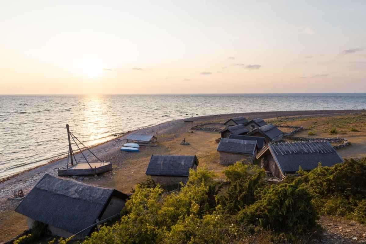 Traditional fishing huts on a stony Öland beach at sunset.