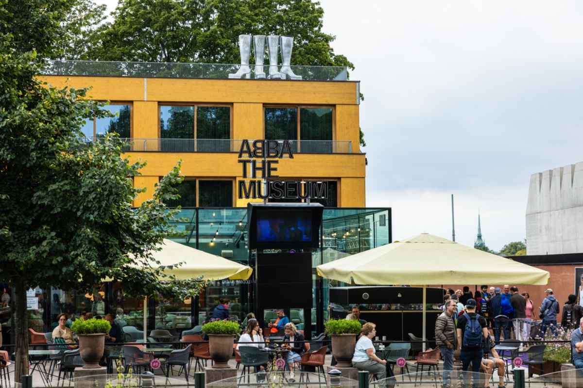 Fasad av ABBA-museet i Stockholm med roliga glänsande stövlar på taket och människor nedanför.