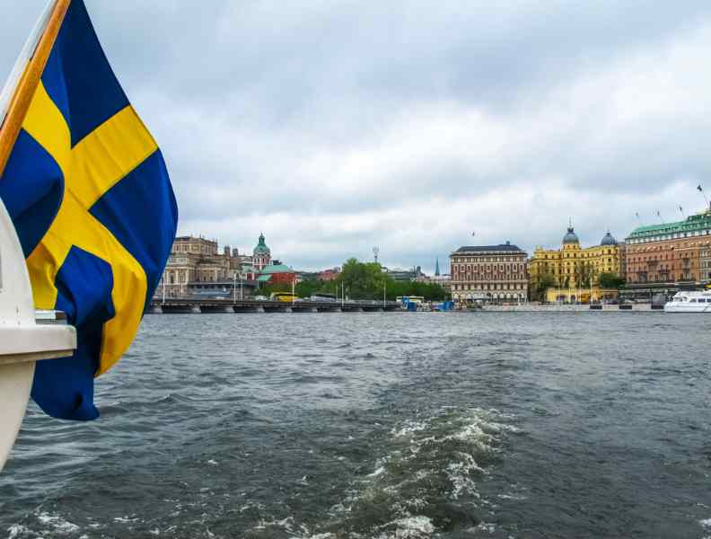Närbild av en svensk flagga som vajar i vinden på fören av en båt som rör sig i vattnet utanför Stockholm.