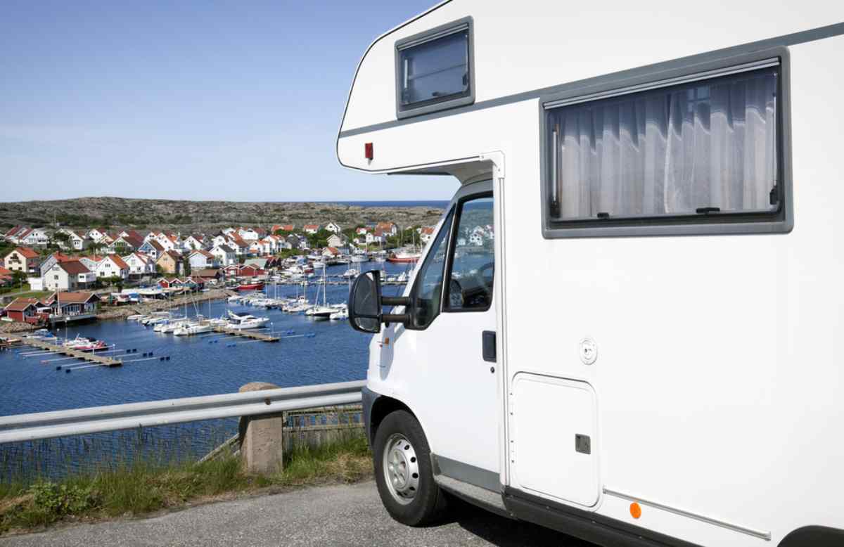 En vit husbil parkerad framför en hamn i Sverige.