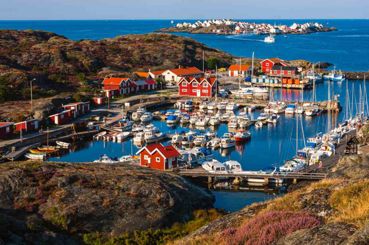 Bohuslän coast fishing harbor with red wooden cottages and dozens of boats in a calm bay on a sunny summer day.