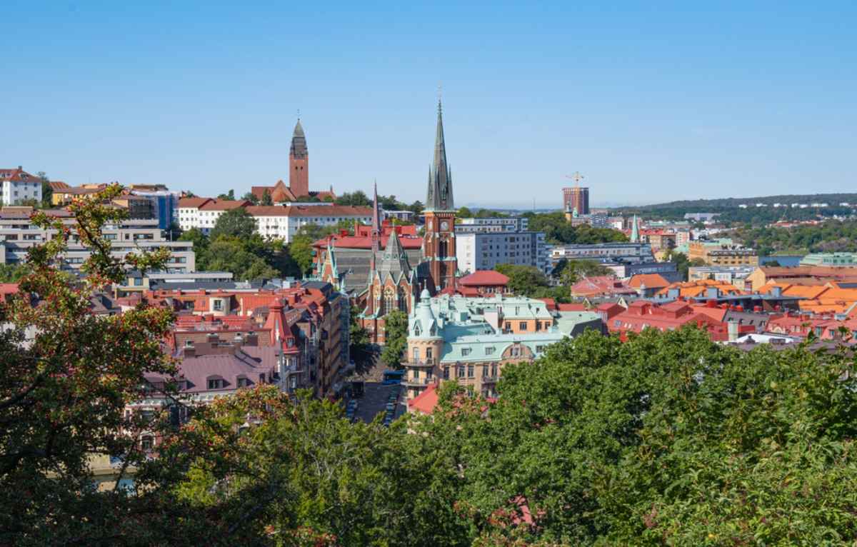 Gothenburg skyline with colorful rooftops and church spires viewed from a hill under a clear blue sky.