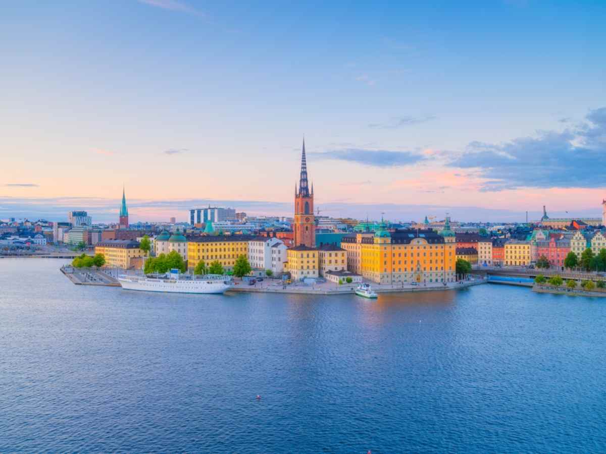 Gamla Stan and Riddarholmen Church spire surrounded by calm harbor waters under a pastel sky.