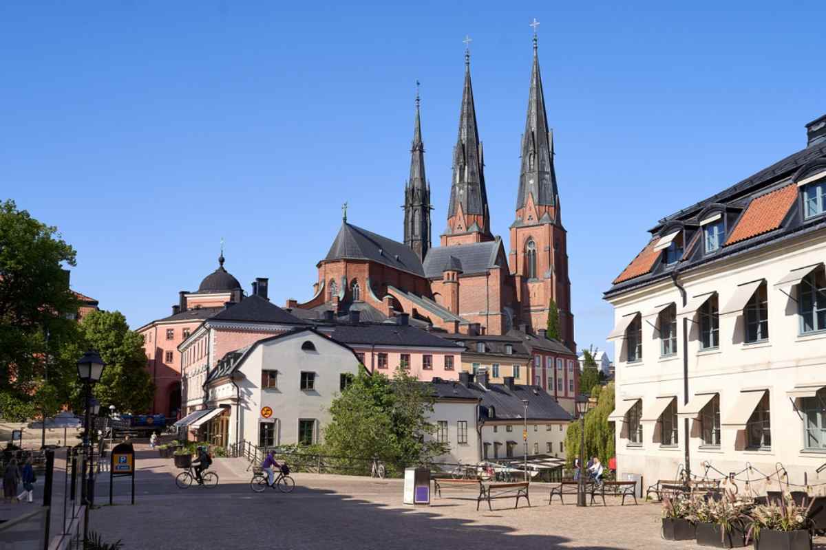 Uppsala Cathedral’s twin spires above a cobblestone square and pastel buildings on a bright, sunny day.