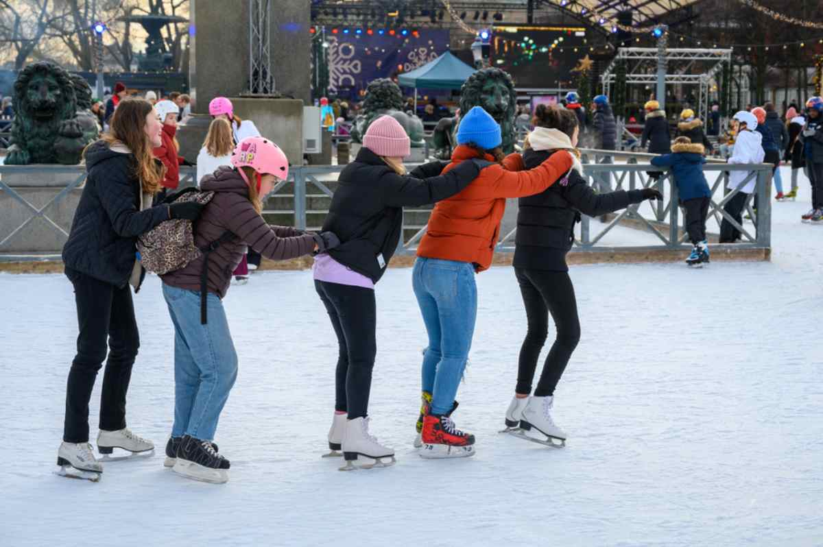 Eine Gruppe Mädchen in Kungsträdgården, Stockholm, die beim Schlittschuhlaufen in einer Reihe stehen und sich an den Hüften halten.