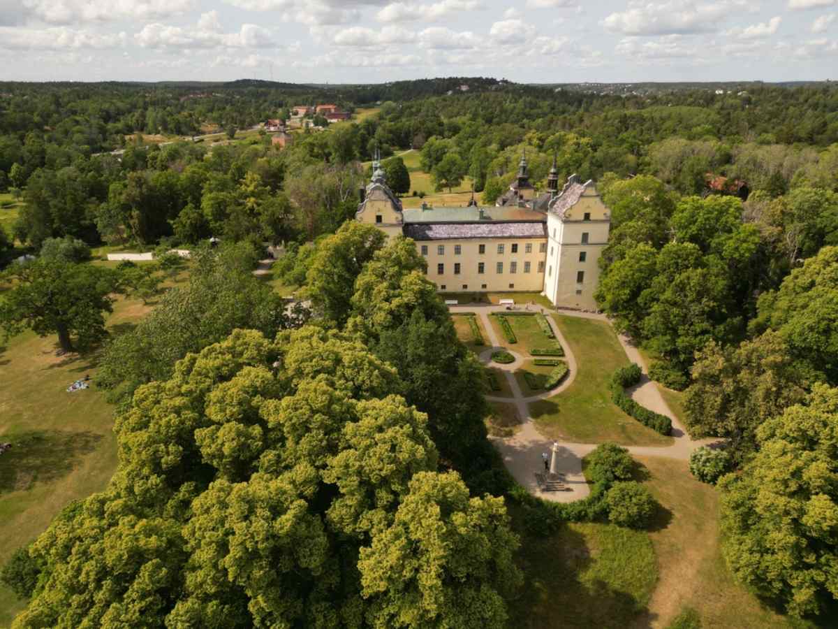 Drohnenaufnahme von Schloss Tyresö in Schweden mit gelblicher Fassade und einer großen grünen Fläche voller Vegetation und Gärten.