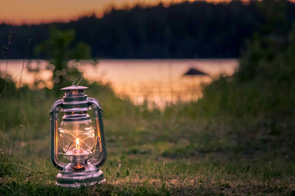 Leuchtende Vintage-Laterne auf einem grasbewachsenen Campingplatz am See bei Sonnenuntergang in Schweden.