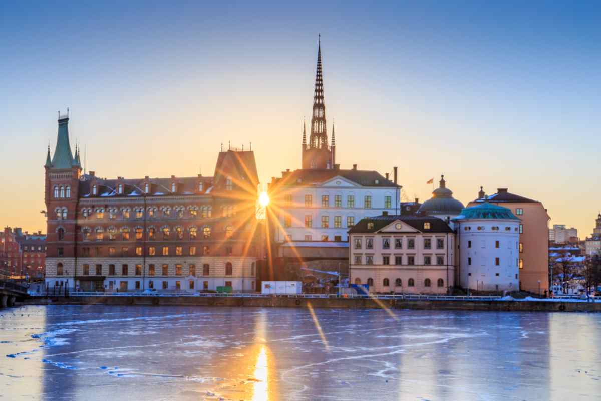 Sonnenuntergang hinter den historischen Gebäuden auf Riddarholmen in Stockholm, mit gefrorenem Wasser im Vordergrund.