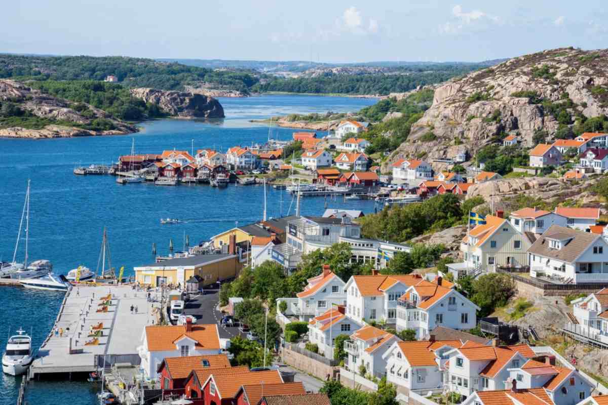 Luftaufnahme der schwedischen Stadt Fjällbacka, bei der du einen Teil der Stadtsilhouette in der Nähe des großen Gewässers, das sie umgibt, und die charakteristischen rötlichen Dächer der Stadt sehen kannst.
