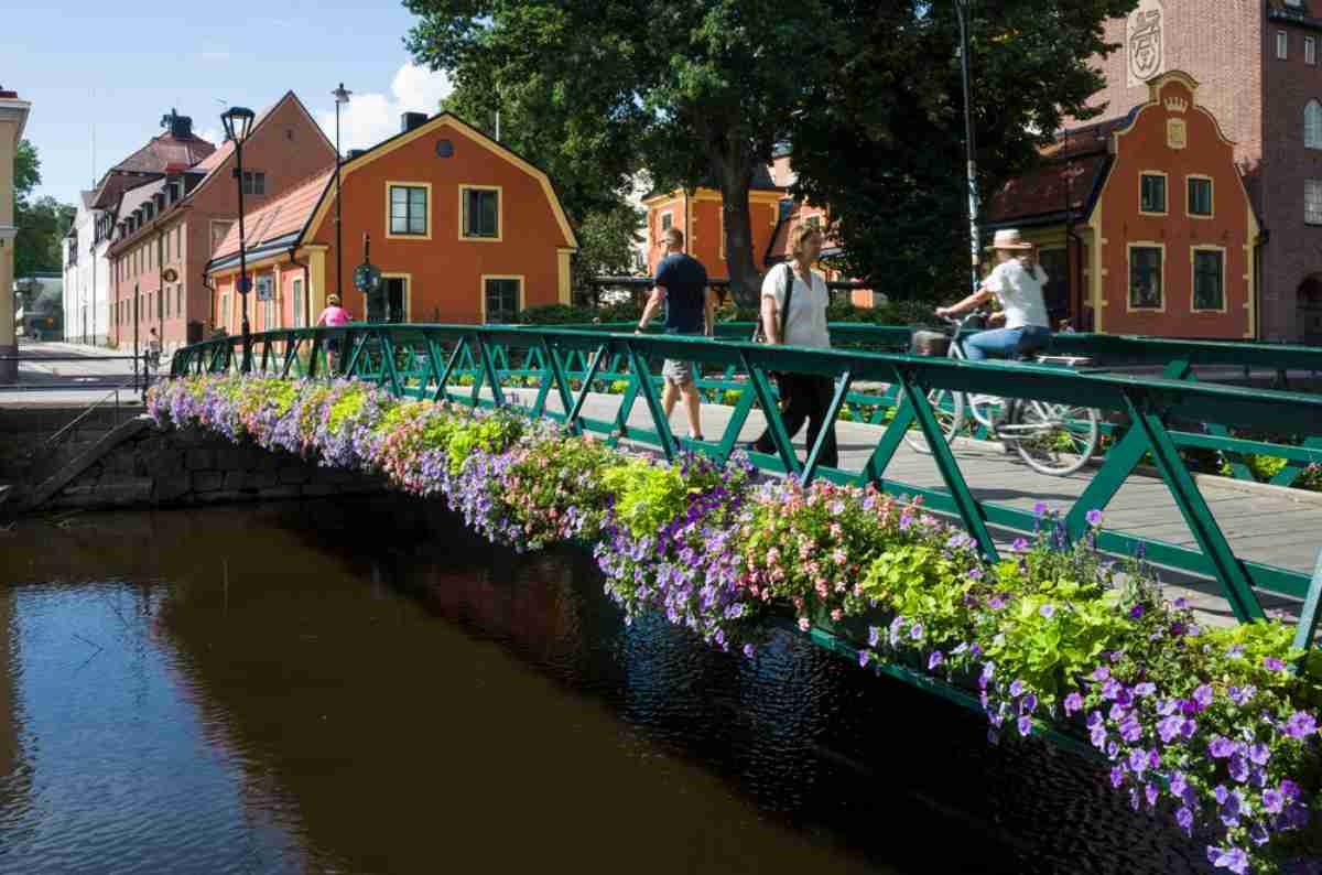 Eine Gruppe von Menschen überquert eine kleine Brücke in der Stadt Uppsala über einen Fluss, umgeben von wunderschönen Frühlingsblumen.