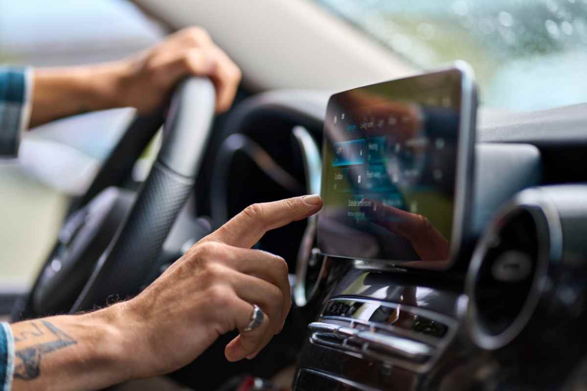 Die Hand eines Mannes berührt den Bildschirm eines Handys, das am Armaturenbrett des Autos gehalten wird, in einem Versuch, es mit einer Roadtrip‑App zu verbinden.