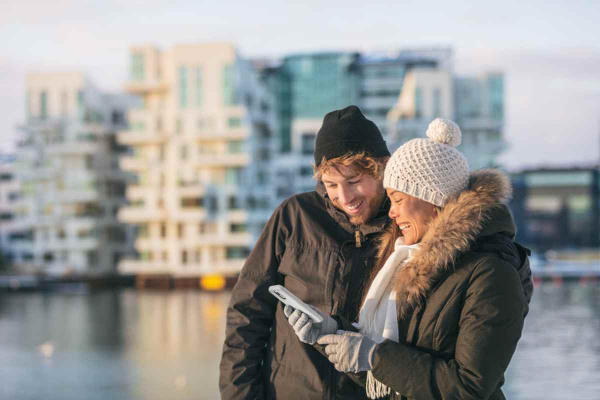 Ett leende par i varma kläder tittar på skärmen på mobiltelefonen som hålls av flickan.