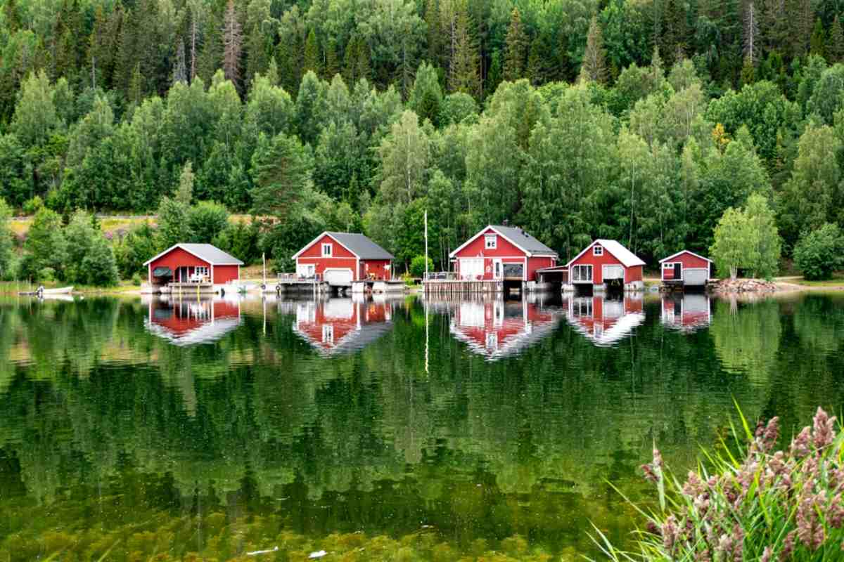 A lake with trees in and around it stretches next to what appears to be a camping cabin in Sweden on a sunny day.
