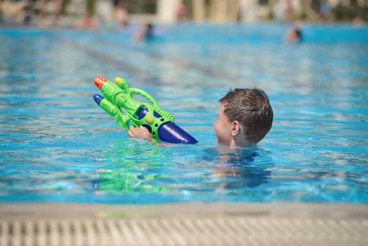 A boy enjoys playing in a swimming pool with a water gun