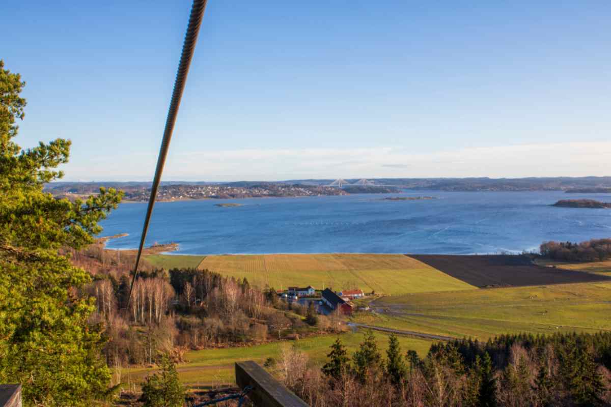 General view of a valley near a large body of blue water in Sweden with a large vegetated esplanade and only human activity on the other side of the shore.