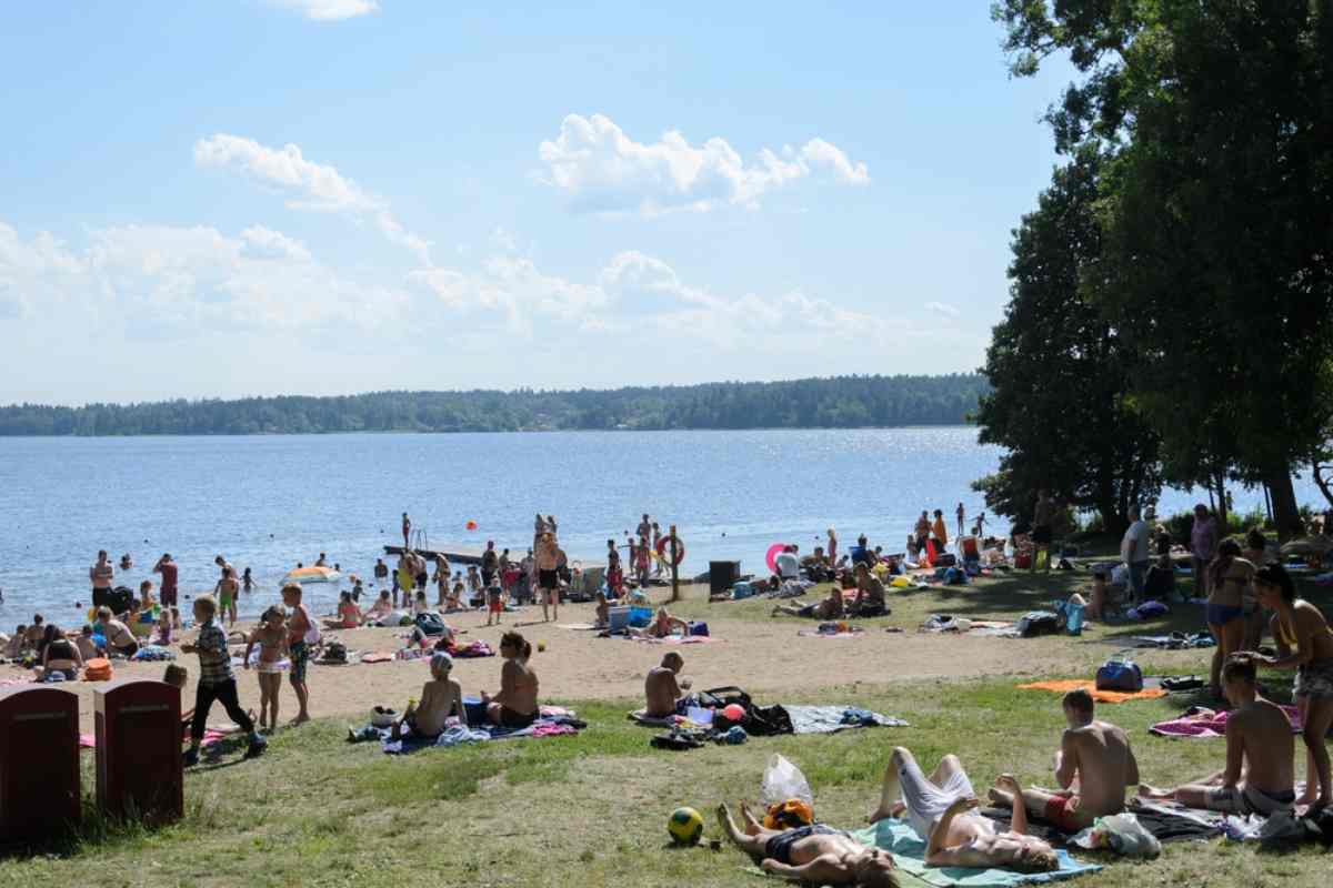 Familien entspannen und sonnenbaden an einem beliebten Strand an einem See bei Stockholm im Sommer
