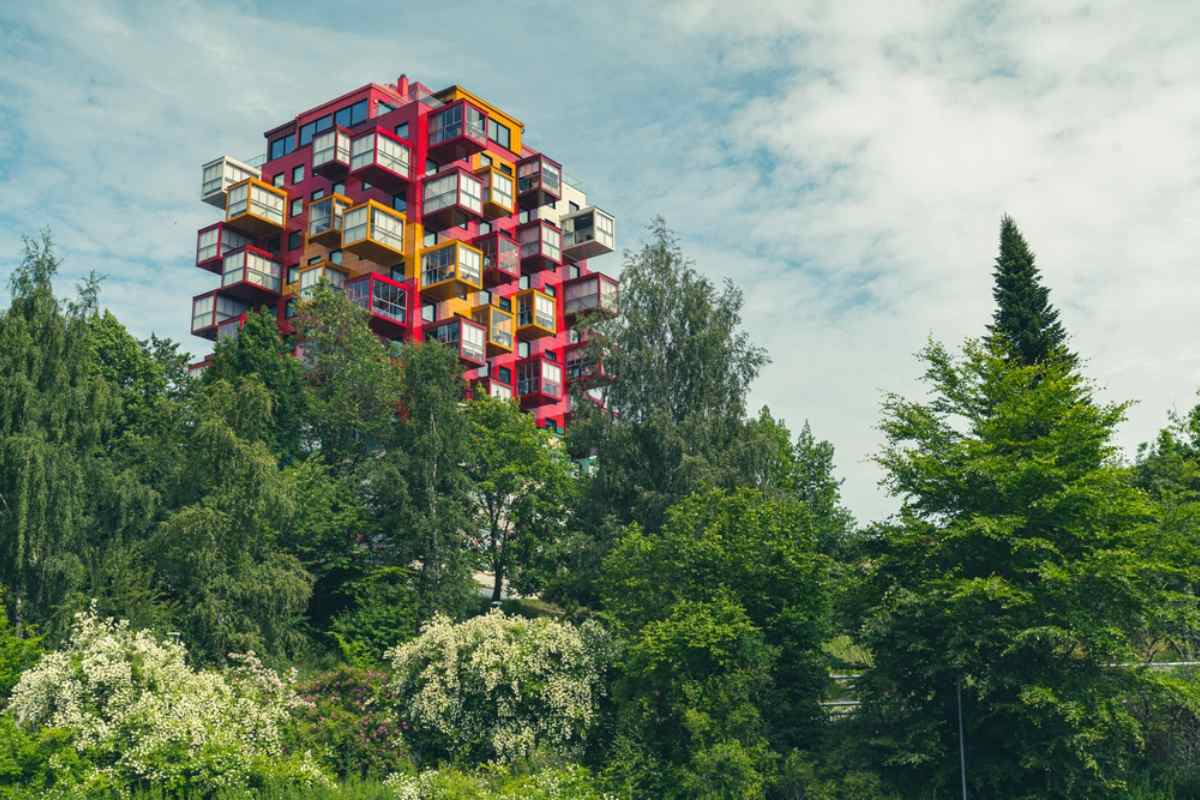Flerfärgat kubformat bostadshus som reser sig ovanför frodig grönska i Örnsköldsvik, ett modernt landmärke vid Sveriges Höga Kusten.