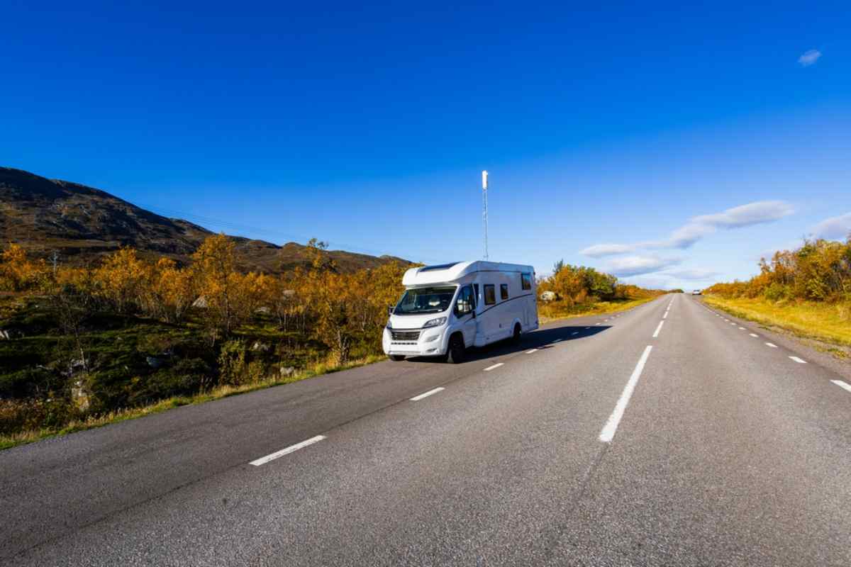 Vit husbil som kör på en tom asfalterad väg genom öppen tundra och höstfärger under klarblå himmel i norra Sverige.