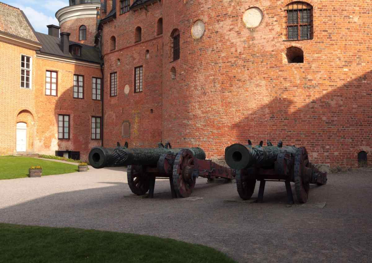 Cannons in the courtyard of Gripsholm Castle's red-brick walls, a historic stop in Mariefred near Lake Mälaren.