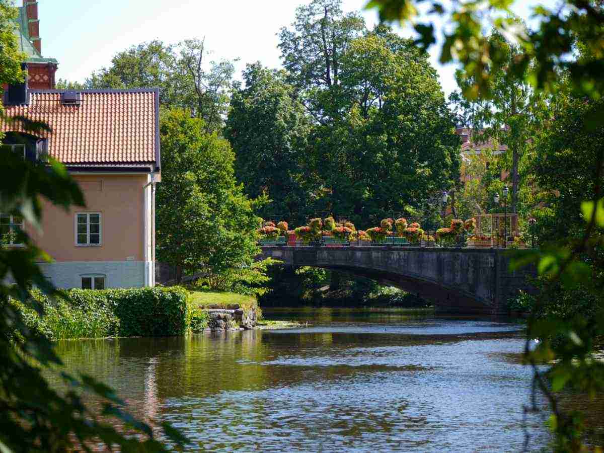 Flower-lined bridge over the Nyköping River with historic houses and lush greenery, a pretty stop on a road trip from Stockholm.
