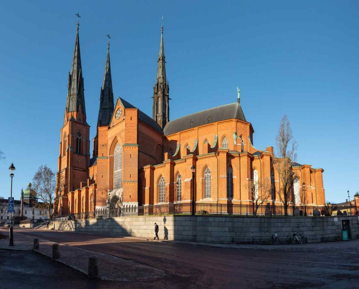 Uppsala Cathedral's twin spires and red-brick facade under a clear sky, an iconic landmark on a day trip from Stockholm.