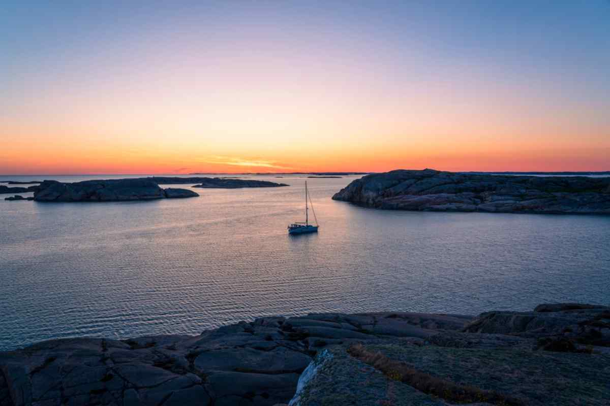 Schwedens Bohuslän-Küste Felsige Küste in Bohuslän bei Sonnenuntergang, mit einem kleinen Segelboot, das zwischen glatten Granitinseln ankert.