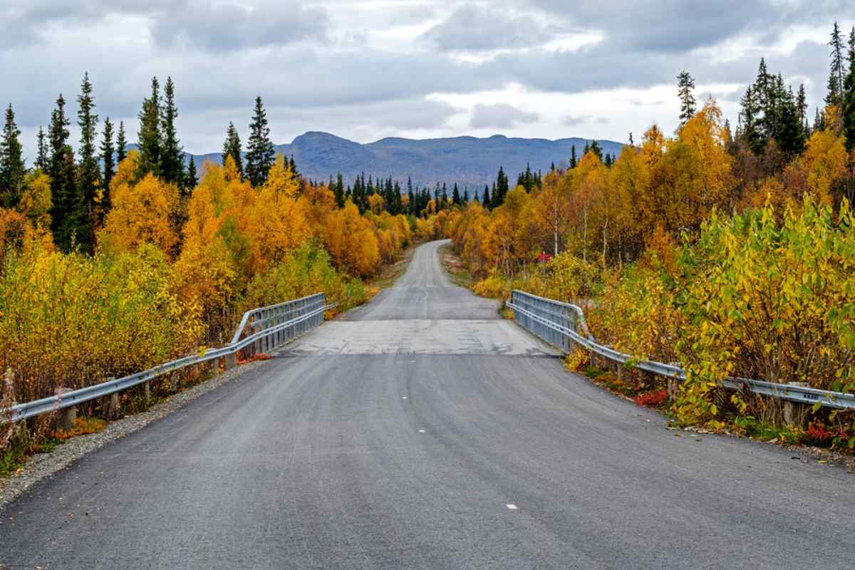 Ruhige Landstraße über eine Brücke mit Herbstbäumen und Bergen in der Ferne in Schweden.